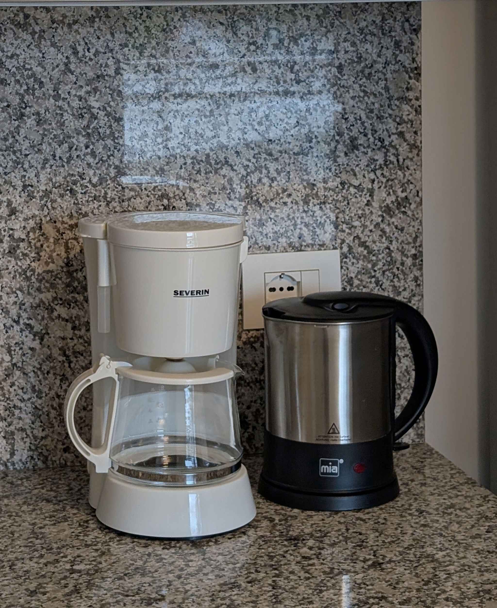 Eine Kaffeemaschine und ein Wasserkocher auf einer Granitarbeitsplatte.