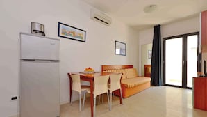 A compact living space with a kitchenette, a dining area with a table and chairs, a sofa, and a large window.