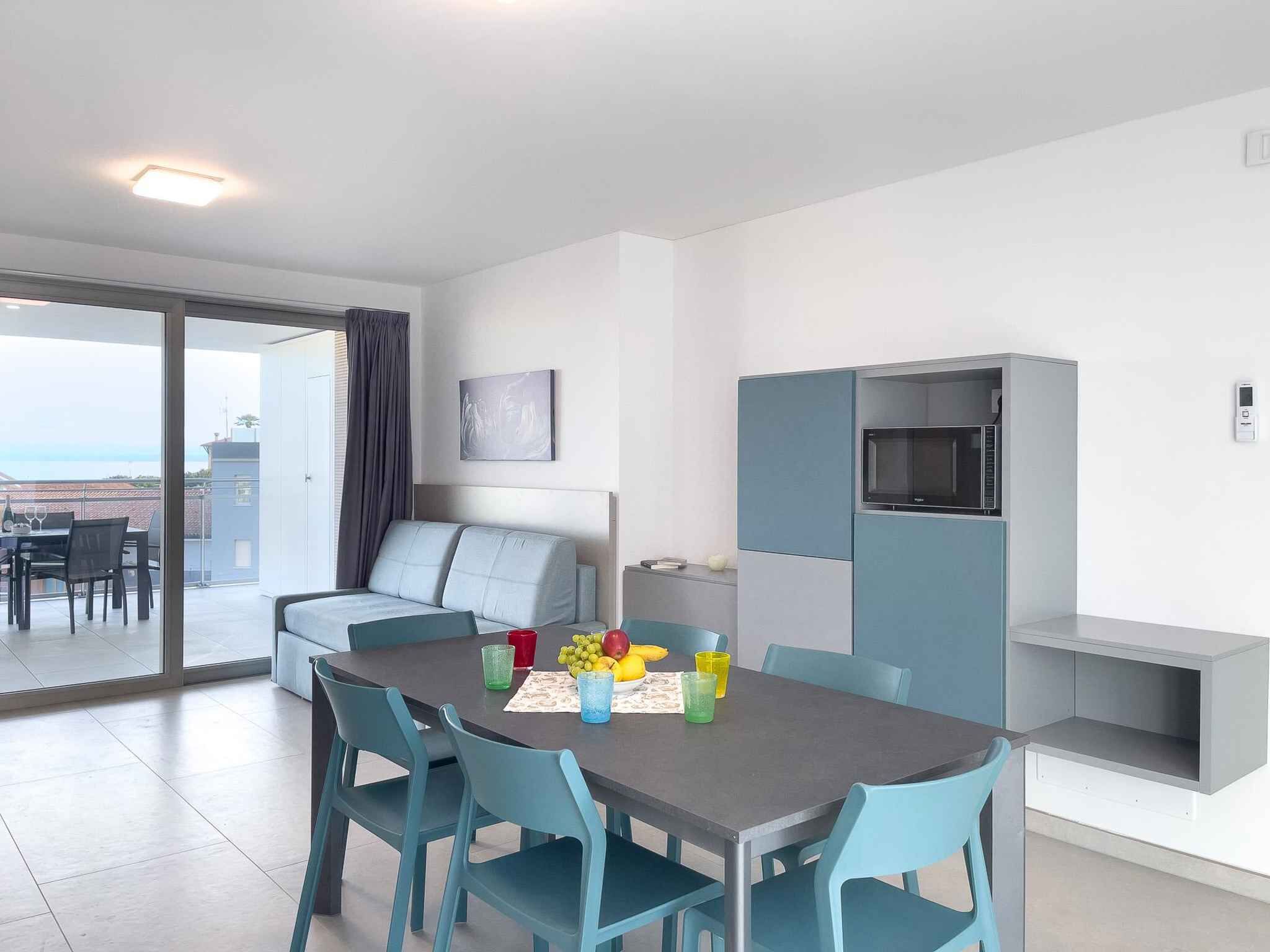 A modern living room with a sofa, dining table, and chairs. There is a TV on a stand and a window with curtains.
