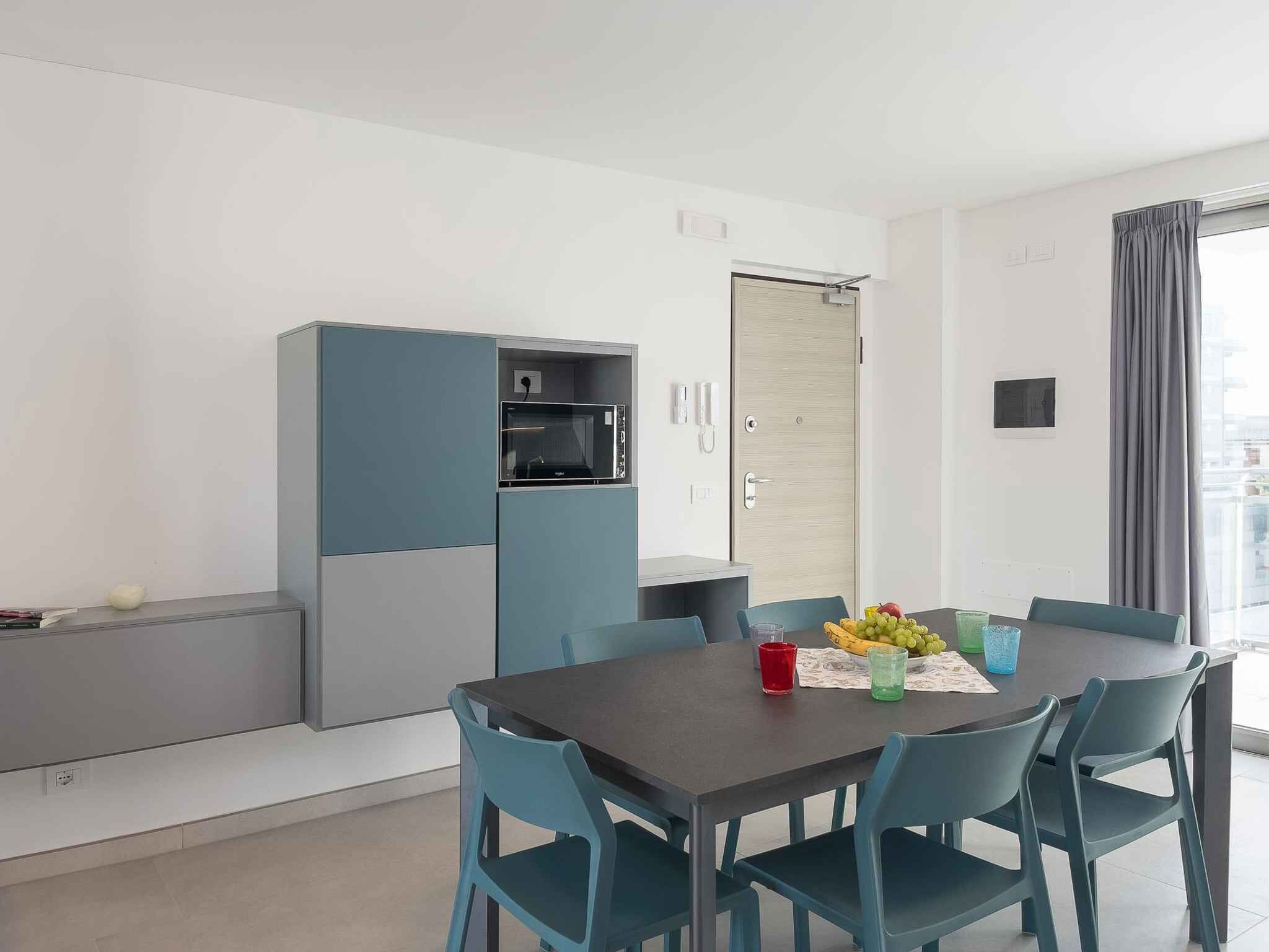 A modern dining area with a table set for four, a microwave, and a refrigerator in the background.