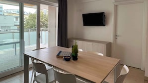 Ein modernes Zimmer mit einem Holztisch, zwei weißen Stühlen, einer Topfpflanze und einem an der Wand befestigten Flachbildfernseher.