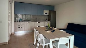 Eine moderne Küche mit grauen Schränken, einer Mikrowelle und einem Spülbecken. Im Wohnbereich befindet sich ein Esstisch mit Stühlen und ein blaues Sofa.
