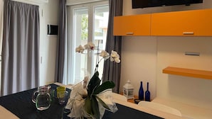 Ein modernes Zimmer mit einem Flachbildfernseher, einem Sofa und einem Esstisch mit einer Orchideen-Vase.