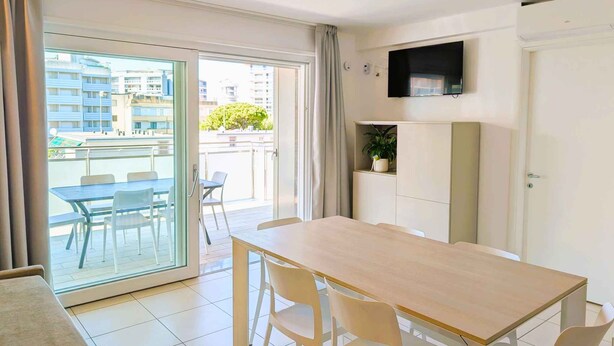 A modern apartment with a dining area, a TV mounted on the wall, and a balcony with a view of the city. - Holiday apartment with balcony and air conditioning (Lignano)