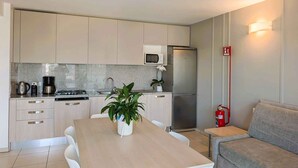 A compact kitchen with a microwave, stove, and refrigerator, a dining table with chairs, and a sofa. - Holiday apartment with balcony and air conditioning (Lignano)