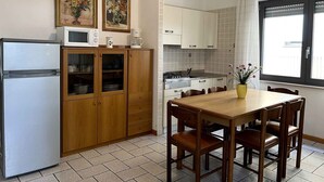 Une cuisine compacte équipée d’un réfrigérateur, d’un four à micro-ondes et de meubles de rangement en bois. On y trouve une table à manger avec des chaises, ainsi qu’une fenêtre avec des rideaux.