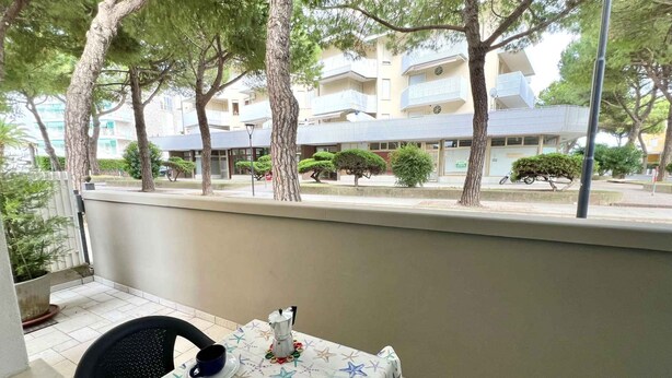 Une terrasse extérieure avec une table dressée pour deux personnes, entourée d’arbres et offrant une vue sur des immeubles d’habitation.