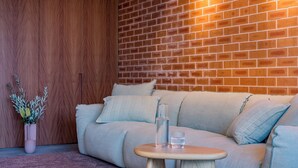 Una sala de estar moderna con pared de ladrillo, un guardarropa de madera, un sofá beige y una pequeña mesa de madera con dos vasos de agua.