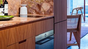 Una cocina moderna con salpicadero de piedra, armarios de madera y horno empotrado. Hay una botella de vino y un florero en la encimera.
