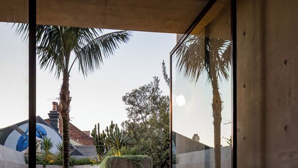 Un espacio exterior moderno con suelo de hormigón, paredes de vidrio y una zona de estar con sillas y una mesa.