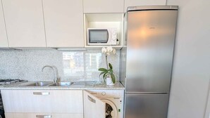 A compact kitchen with a stainless steel refrigerator, a microwave, a sink, and a washing machine. - Holiday flat with balcony and air conditioning (Lignano)