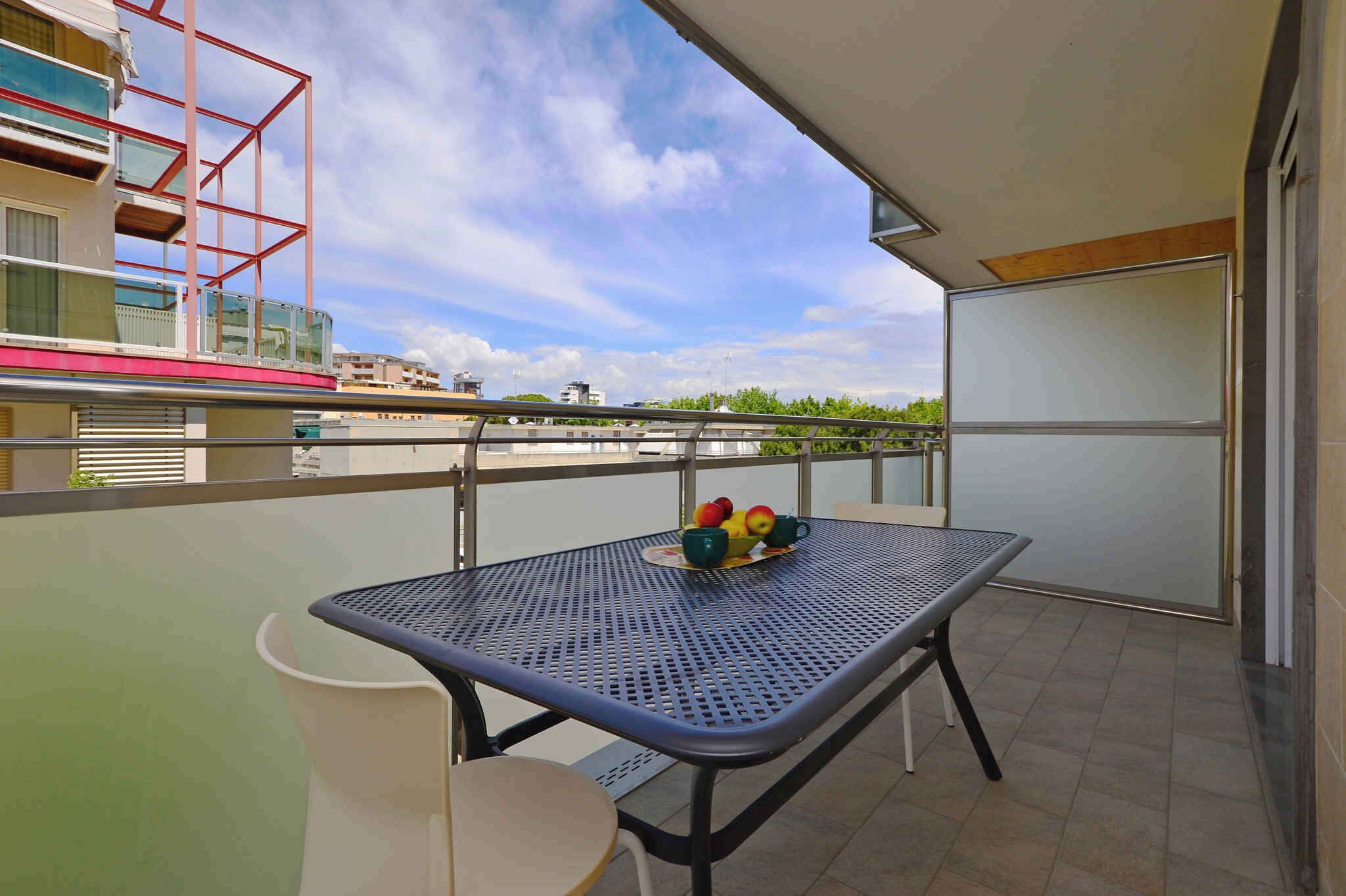 A balcony with a table and chairs, a bowl of fruit, and a view of buildings and greenery.