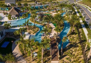 Vue aérienne d’un complexe hôtelier doté d’une grande piscine, de palmiers et d’une structure à toit de chaume.