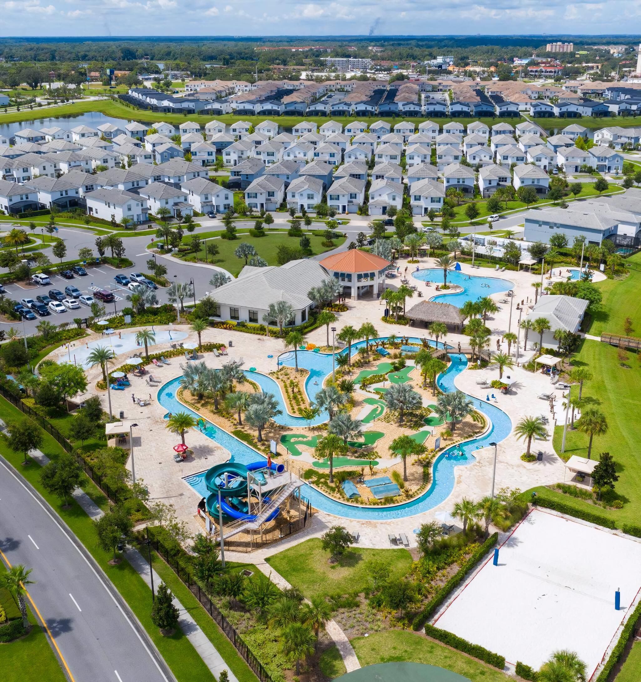 Vue aérienne d’un quartier résidentiel avec un complexe de piscines comprenant un toboggan aquatique et plusieurs bassins.
