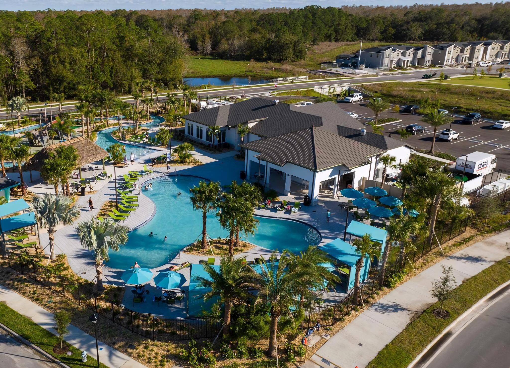 An aerial view of a resort with a large swimming pool, multiple lounge areas, and a parking lot.