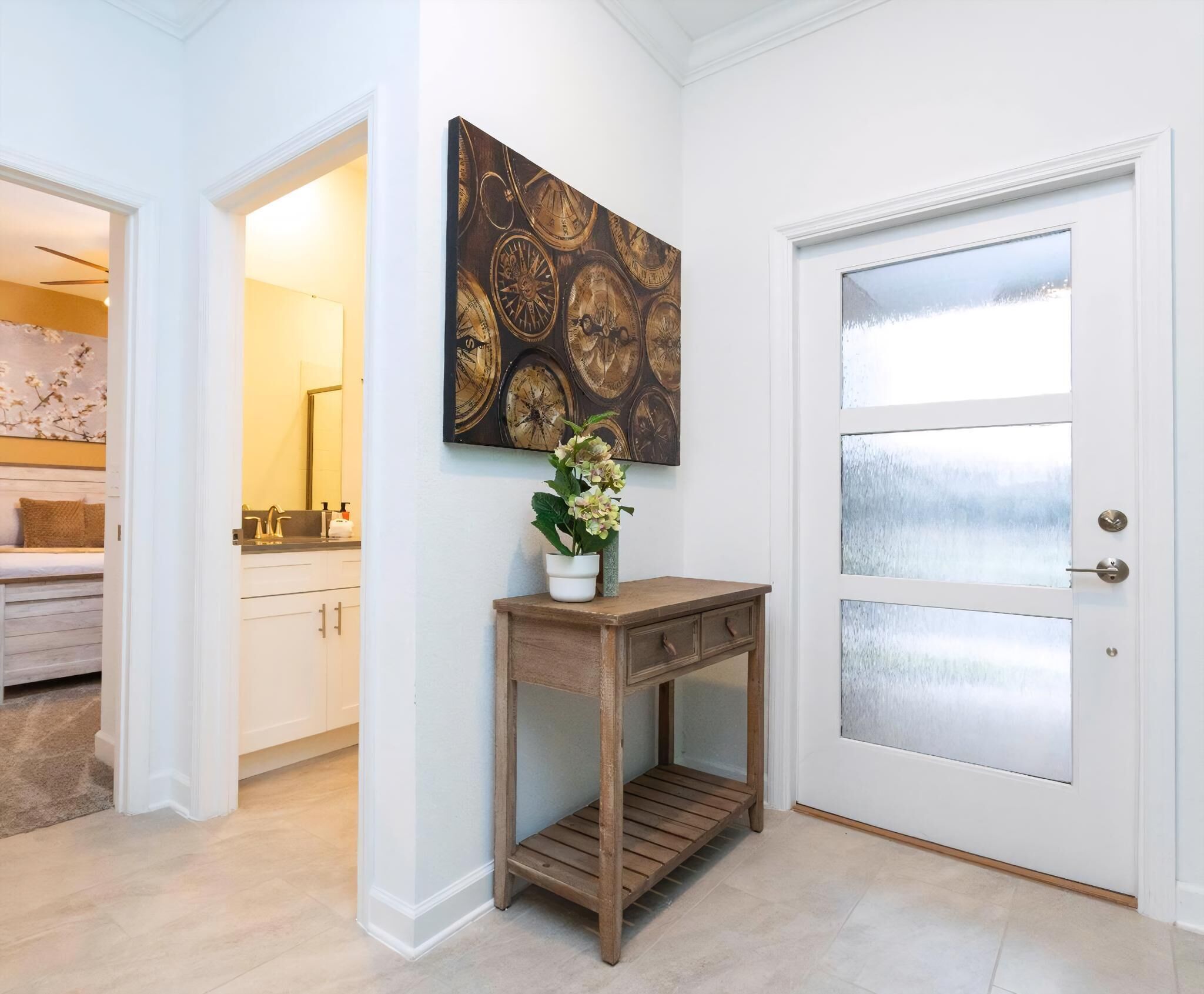 Un couloir avec une porte blanche, une console en bois sur laquelle est posée une plante en pot, et une œuvre d’art accrochée au mur.