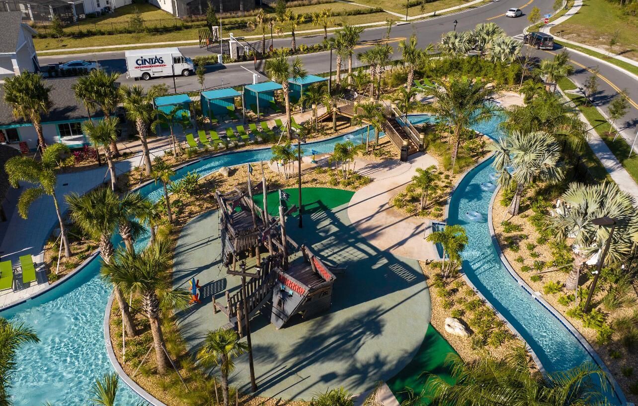 An aerial view of a resort with a pool area, palm trees, and a road with vehicles.
