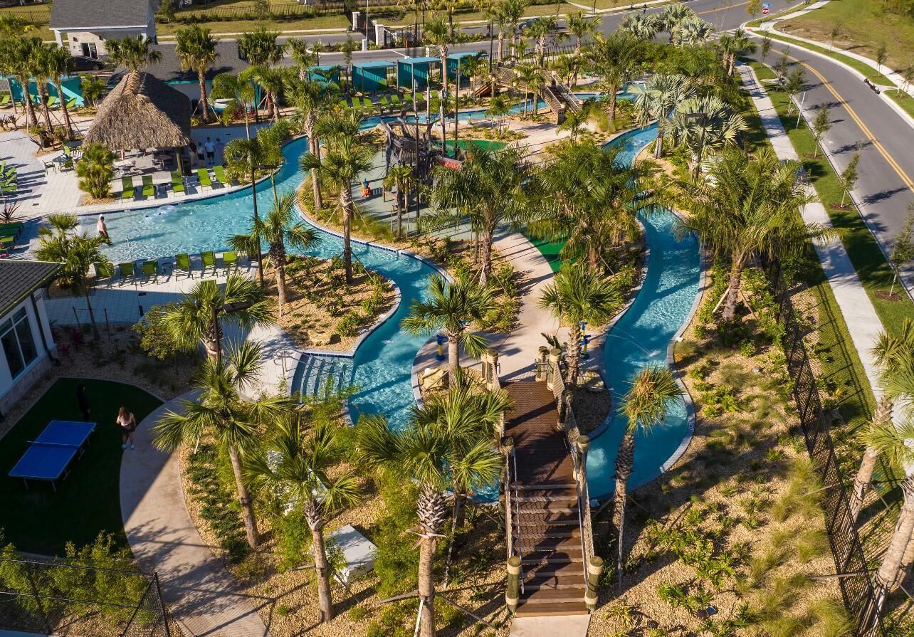 Vista aérea de un complejo turístico con una gran piscina, palmeras y una estructura de techo de paja.