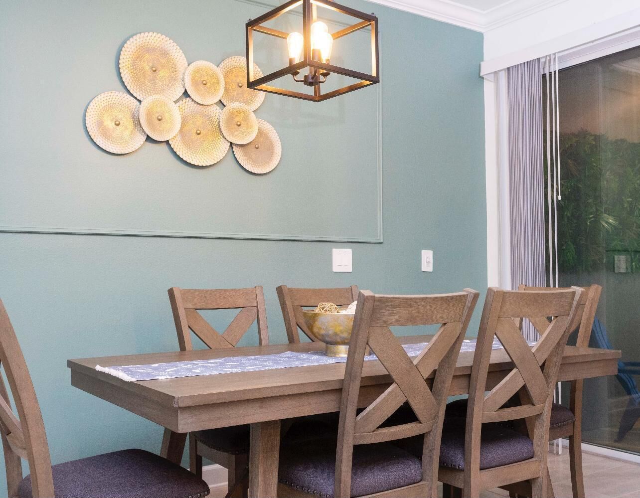 A dining area with a wooden table and chairs, a decorative wall piece, and a hanging light fixture.