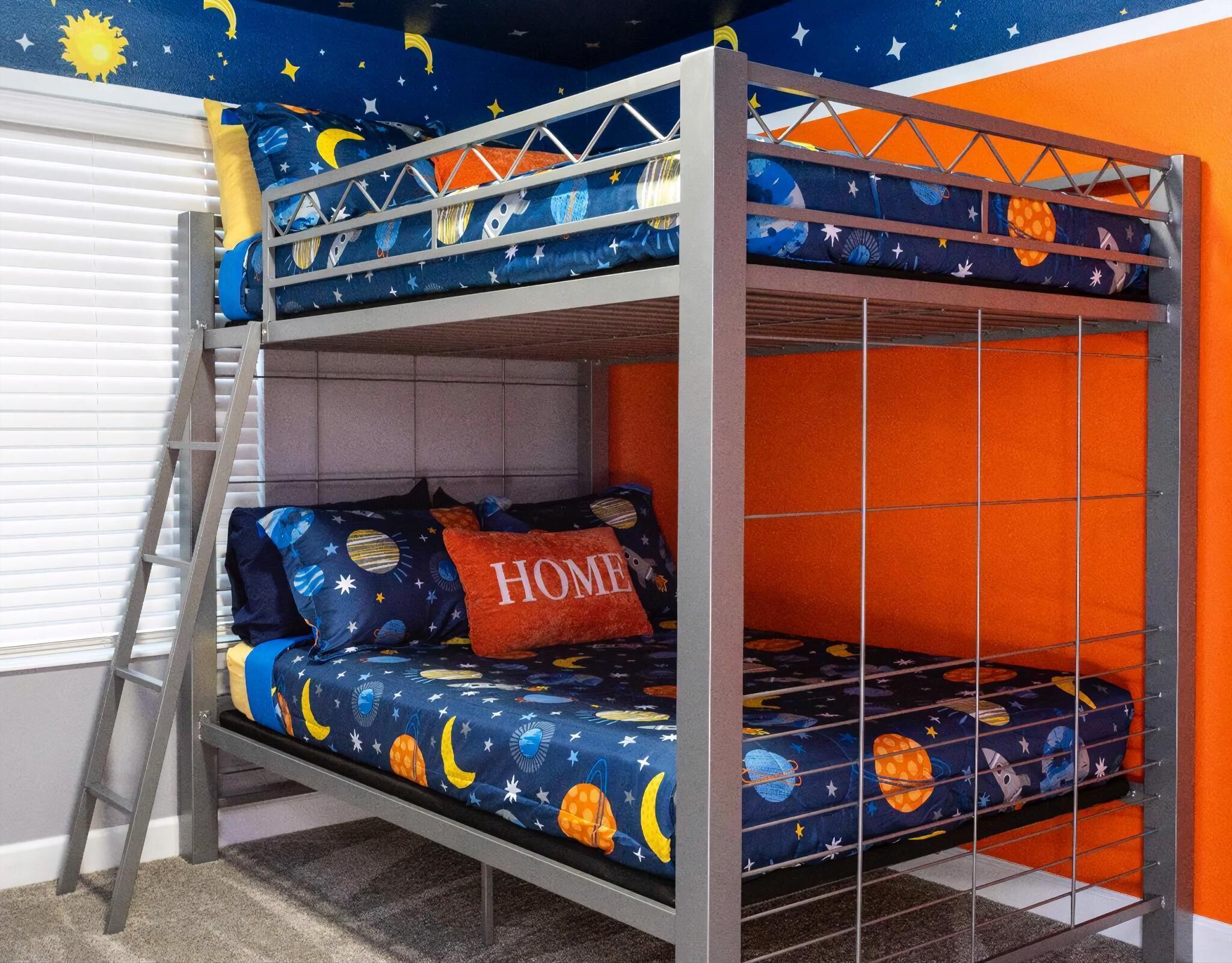 A bunk bed with a space-themed mattress cover, a ladder, and a pillow with "HOME" on it.