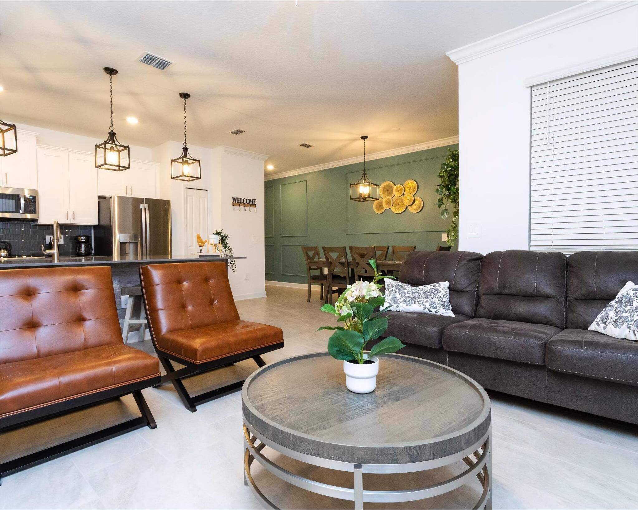 A modern living room with a leather sofa, a round coffee table, and a dining area in the background.