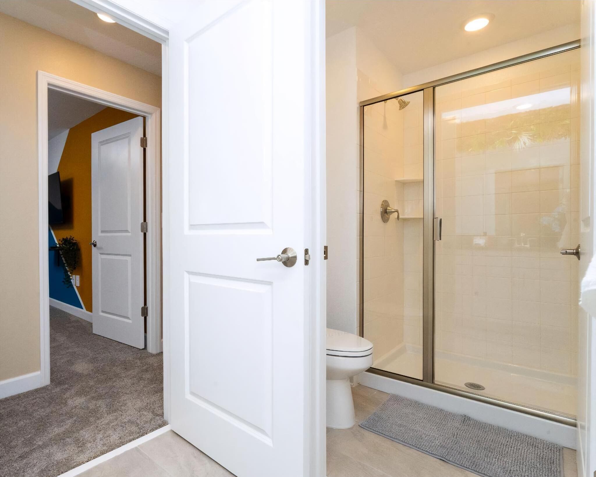 A bathroom with a glass-enclosed shower, a toilet, and a white door.