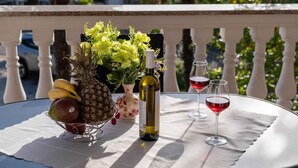 Ein Tisch mit einer Obstschale, einer Weinflasche und zwei Weingläsern auf einem Balkon.