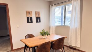 A dining area with a wooden table, four brown chairs, a potted plant, and two wall-mounted artworks.