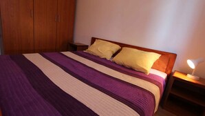 Un lit avec une couvre-lit à rayures, deux oreillers, une armoire en bois et une lampe de chevet.