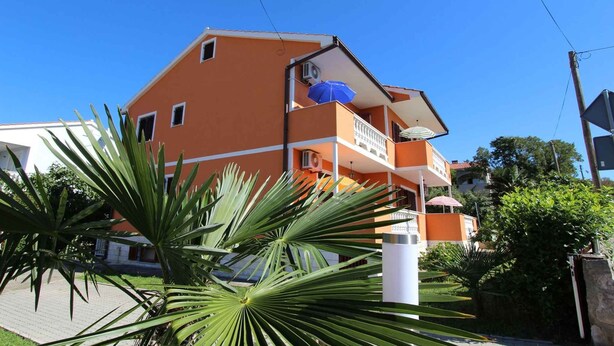 Un immeuble à plusieurs étages, doté de balcons, se dressant sous un ciel d’un bleu limpide.