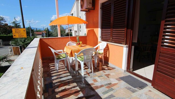Un área de estar al aire libre con mesa y sillas, piso de baldosas y un letrero que indica las direcciones a lugares cercanos.
