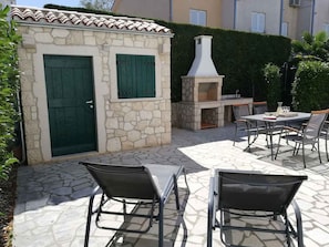Eine Terrasse im Freien mit Steinböden, einer Steinwand, einer grünen Tür und einem Barbereich mit Kamin.
