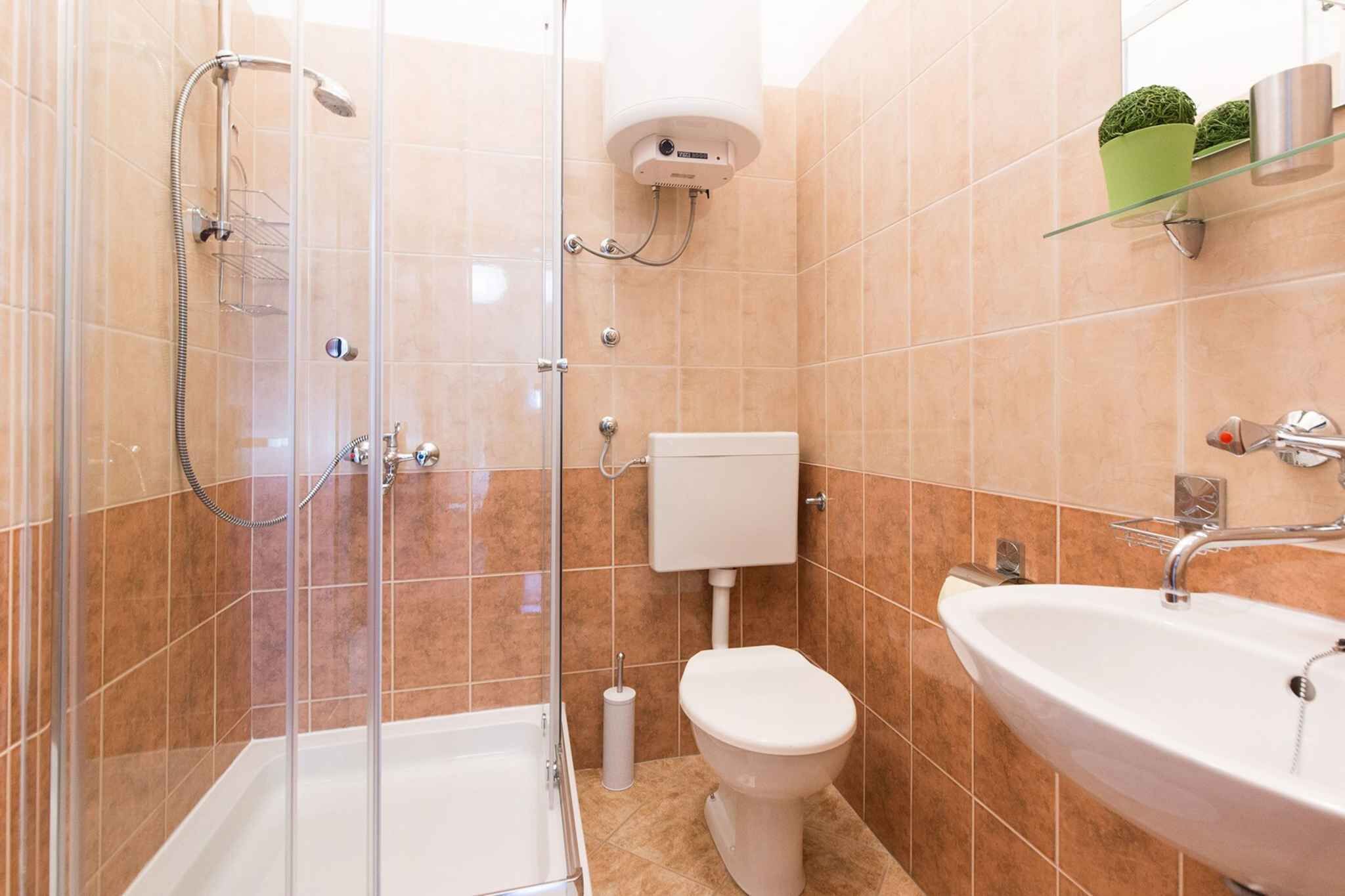 A bathroom with a glass-enclosed shower, a toilet, a sink, and a toilet paper holder.