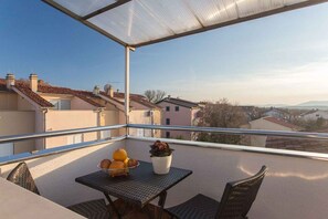 Un balcon avec une table, des chaises, un pot de fleurs et un panier de fruits.