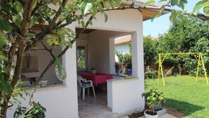 A covered patio area with a table and chairs, surrounded by potted plants and a yellow swing set.