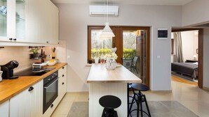 Una cucina moderna con mobili bianchi, un piano di lavoro in legno e un’isola centrale con sgabelli. Si intravede un’area pranzo con tavolo e sedie attraverso una porta in vetro.