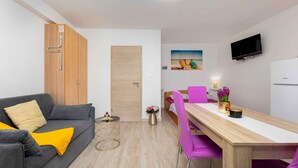 A compact living space with a sofa, a dining table with chairs, a TV mounted on the wall, and a wooden wardrobe with a door. - Studio with pool for 6 people (Malinska)