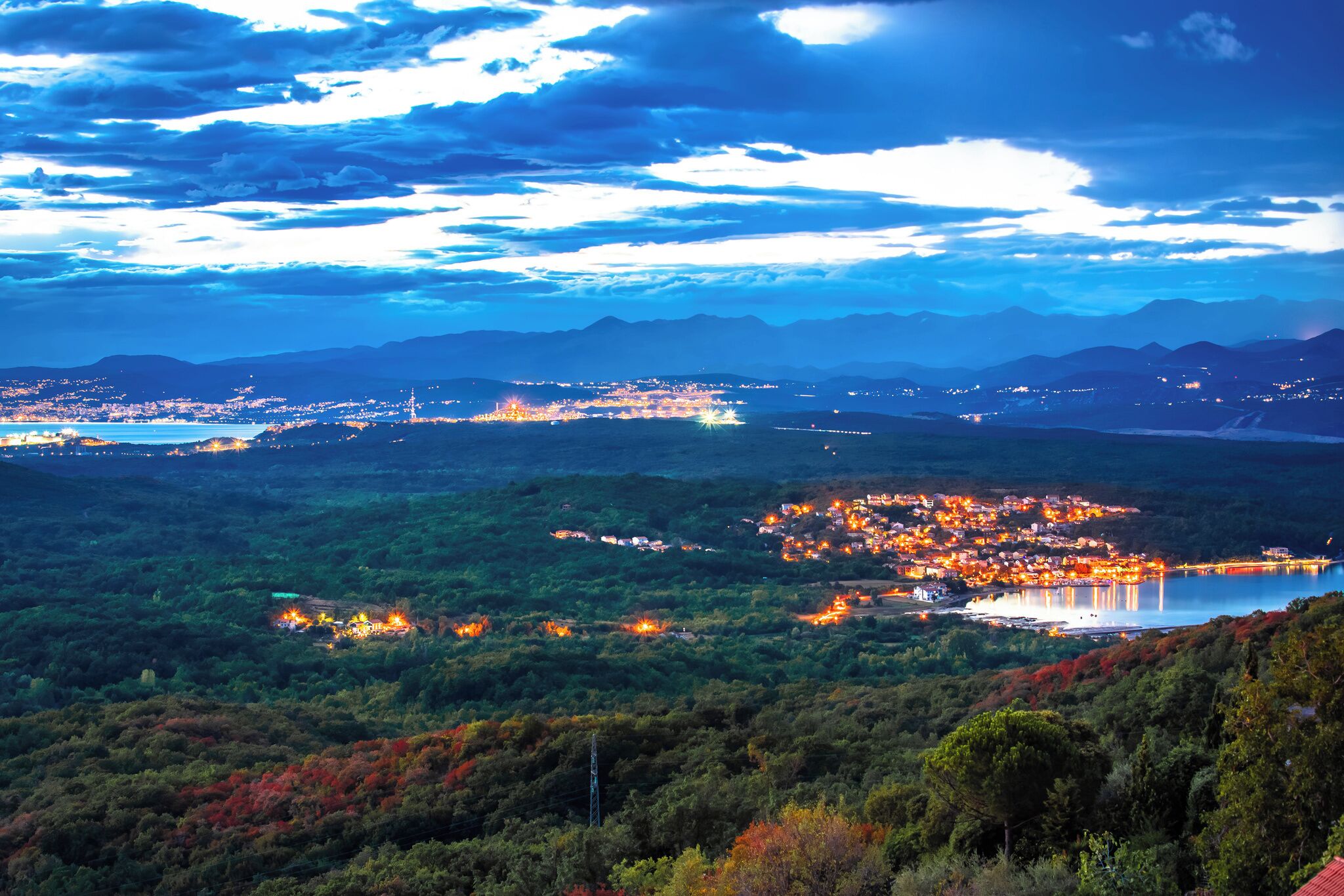 Vista panorámica de un pueblo con un lago, rodeado de montañas y un bosque denso.