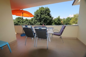 Um pátio com mesa e cadeiras, um guarda-sol laranja e vista para árvores e edifícios.