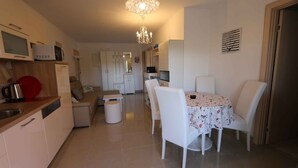 A modern kitchen with white cabinets, a dining area with a table and chairs, and a chandelier. - Holiday apartment with balcony and air conditioning (Šilo)