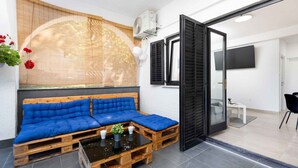 A modern room with a wooden pallet sofa, a small table with cups and a plant, and a large window with black shutters.