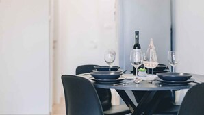 A dining table set with plates, glasses, and a bottle, in a modern room with white walls and black chairs.