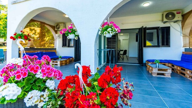 A covered outdoor seating area with white walls, blue sofas, and hanging flower baskets.