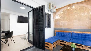 A modern living room with a sectional sofa, a dining area with a table and chairs, and a sliding glass door leading to another room.
