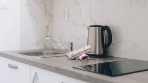 A kitchen with a marble backsplash, a stainless steel kettle, and a rolled-up cloth on the counter.