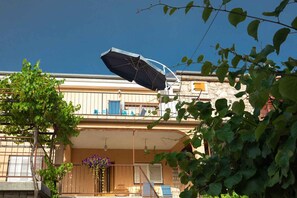 A building with a balcony, a hanging umbrella, and a tree with green leaves.