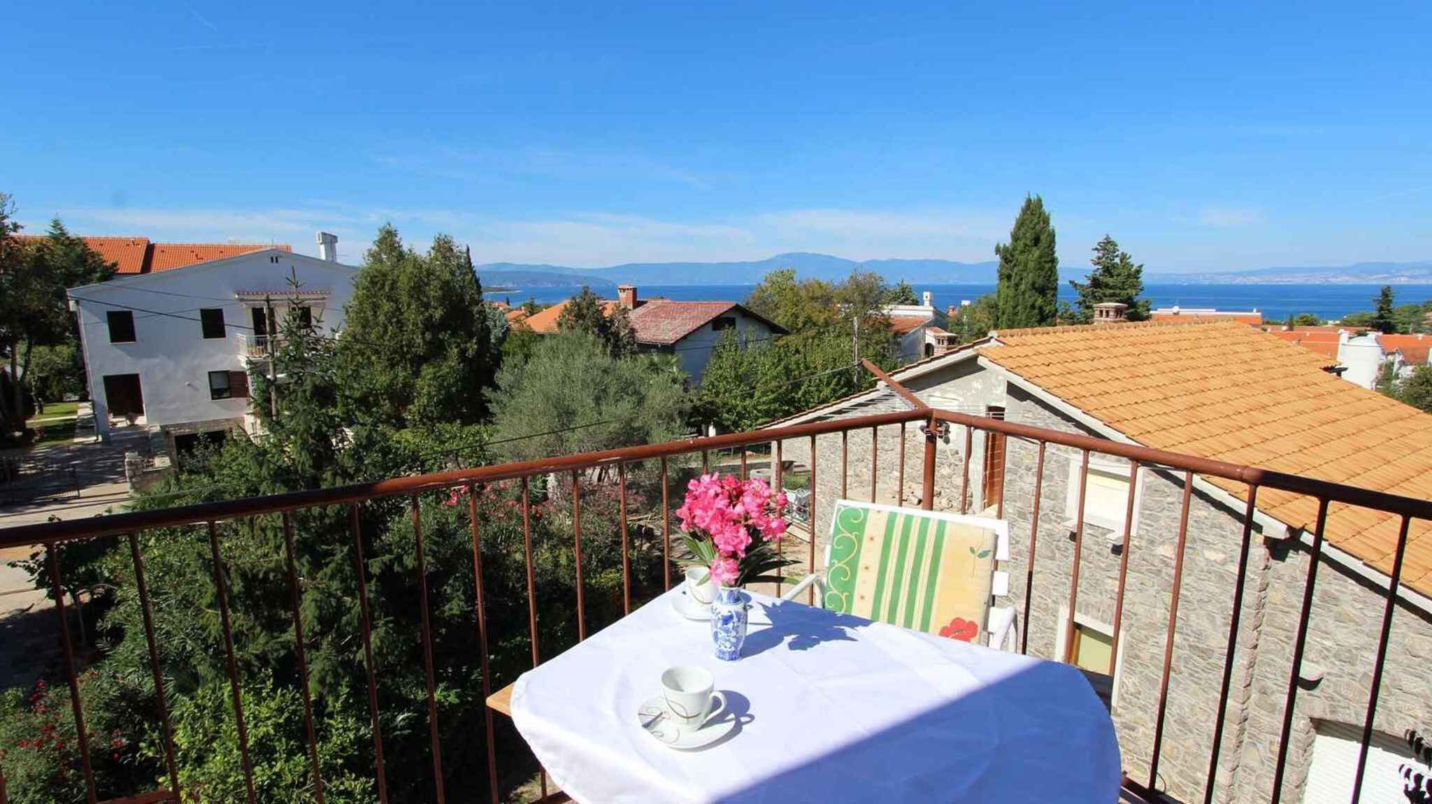 Ein Balkon mit einem für Tee gedeckten Tisch, mit Blick auf ein Küstendorf mit Häusern und blauem Himmel.