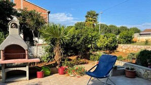 Eine Terrasse mit Grill, Topfpflanzen und einem blauen Stuhl.