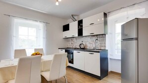 Een moderne keuken met witte kasten, een roestvrijstalen koelkast en een eethoek met een tafel en stoelen.