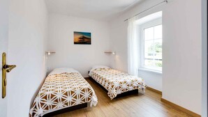 Een kamer met twee bedden, een raam en een schilderij aan de muur.
